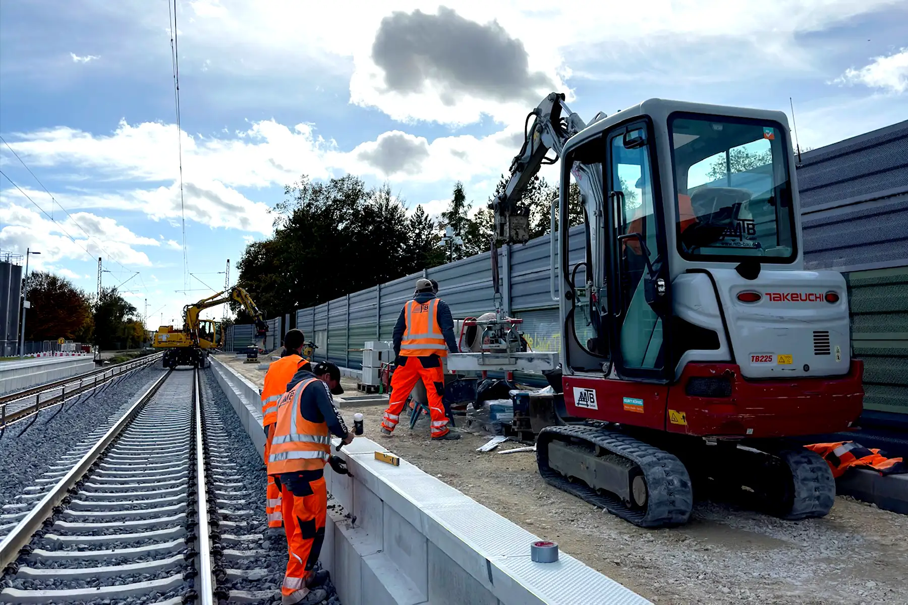 Baustelle am Bahnsteig in Westendorf. Drei Bauarbeiter mit Maschine bei Gleisarbeiten