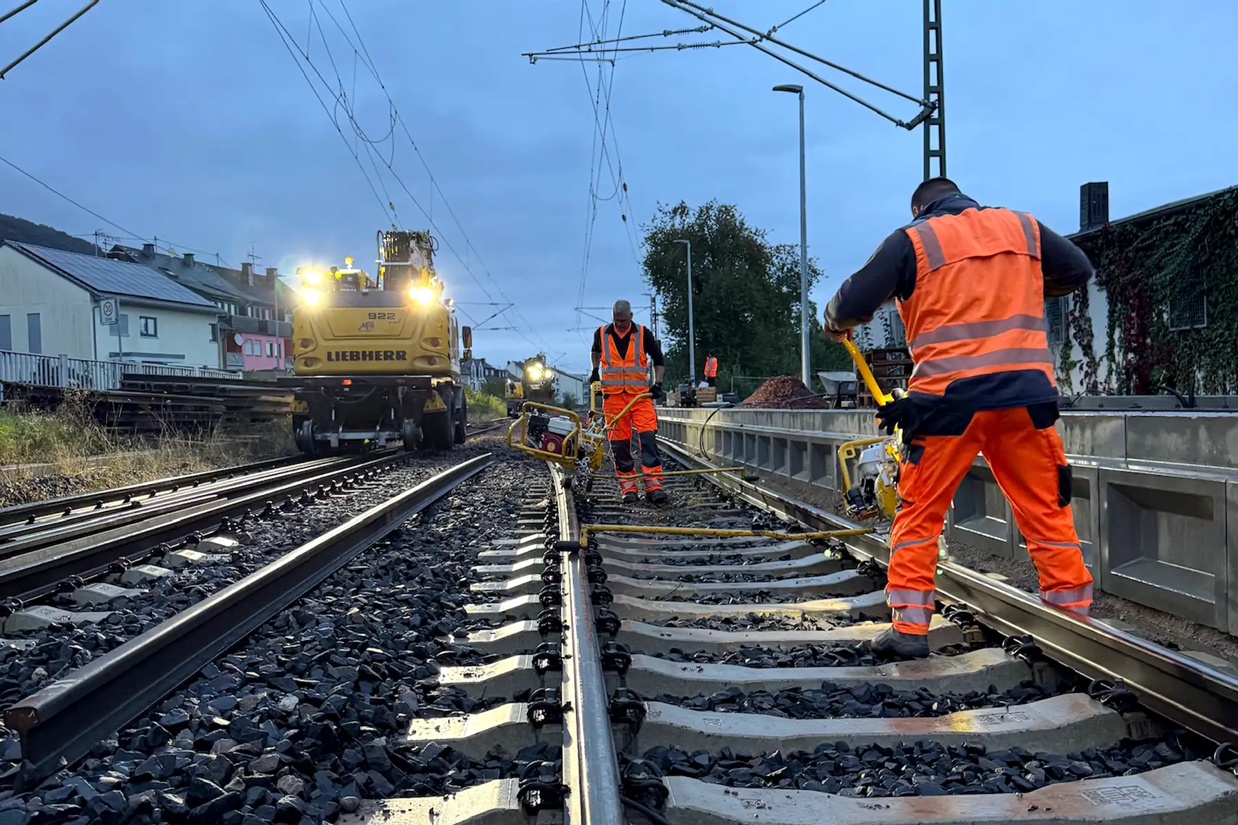 Gleisoberbau in Tier, zwei Bauarbeiter am Abend bei Sonnenuntergang arbeiten mit Maschinen am Gleis