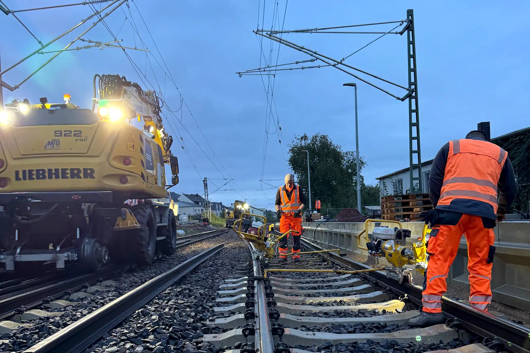Gleisoberbau in Tier, zwei Bauarbeiter am Abend bei Sonnenuntergang arbeiten mit Maschinen am Gleis