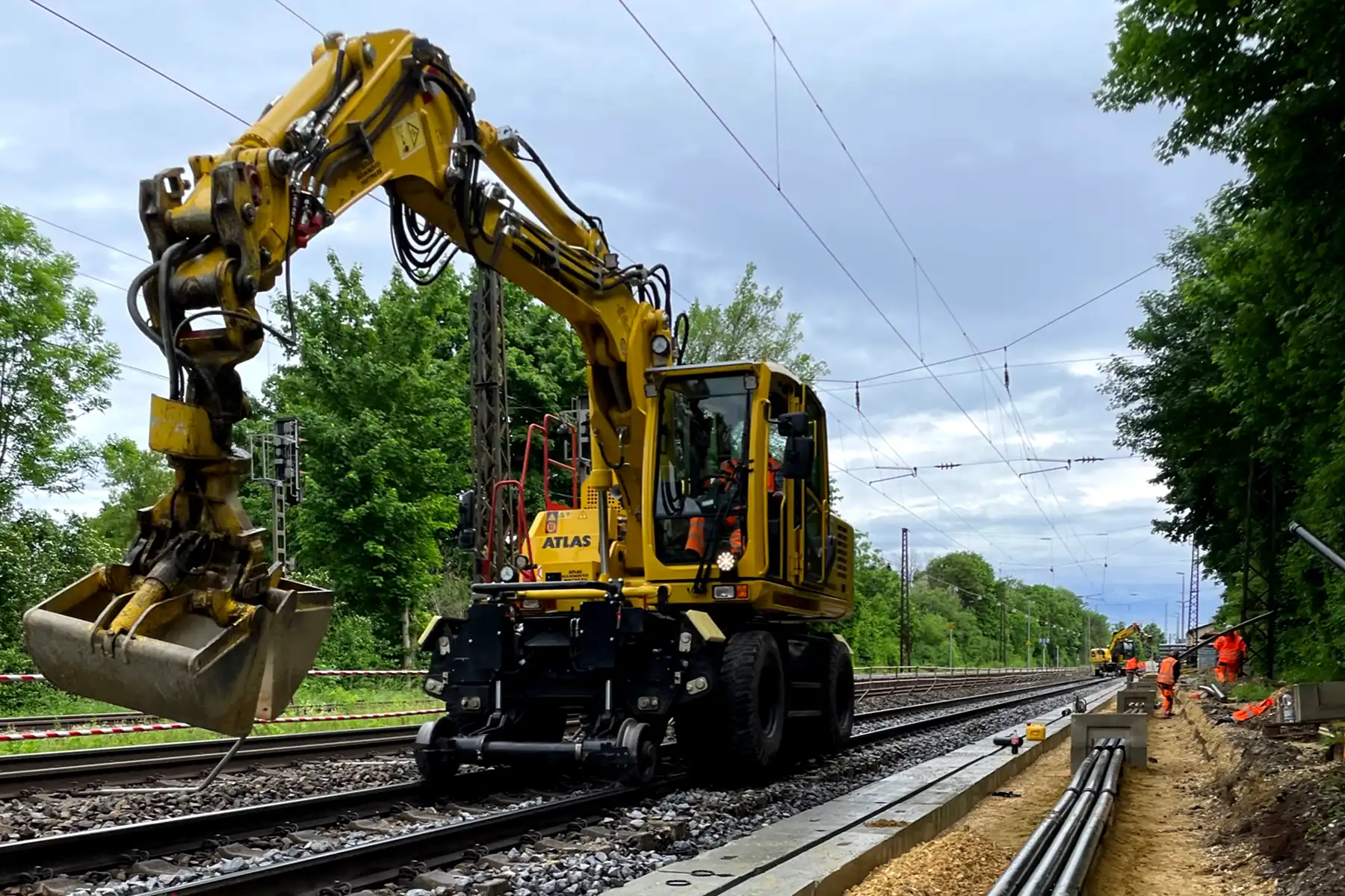 Baggermaschine auf Bahngleis mit Bauarbeitern